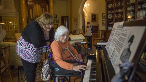 A visitor in a wheelchair plays the piano inside Killerton House with her companion, Devon